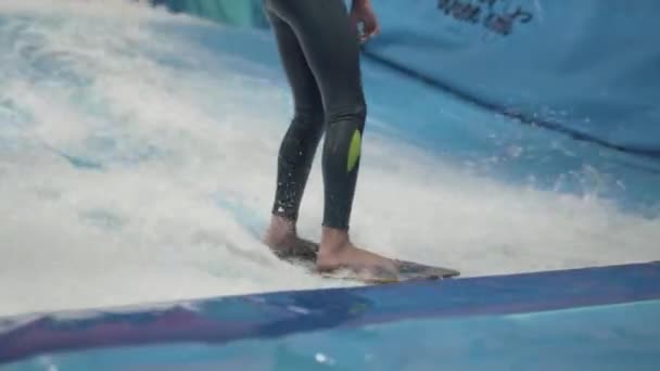 Actividad deportiva acuática, concepto de equilibrio. Pequeño atleta disfrutando del surf indoor. Los paseos adolescentes abordan olas en el simulador en el complejo deportivo. Entrenador de surf y estudiante en sesión en simulador de ola — Vídeo de stock