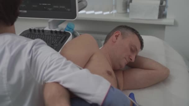 Γιατρός που χρησιμοποιεί μηχάνημα υπερήχων για να σκανάρει την καρδιά ενός άντρα ασθενή. Ο καρδιολόγος κάνει έναν ασθενή ένα ηχοκαρδιογράφημα σε μια κλινική. Ασθενής υπό εξέταση με υπερηχογράφημα στο νοσοκομείο — Αρχείο Βίντεο