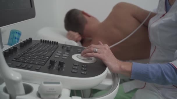 Kadın doktor kalp muayenesi yapıyor. Kardiyoloji kliniğindeki modern ekipmanları kullanıyor. Kadın kardiyolog ultrasonografiyle hastanın kalbini tarıyor. Ekrana bakıyor. Sağlık hizmetleri kavramı — Stok video