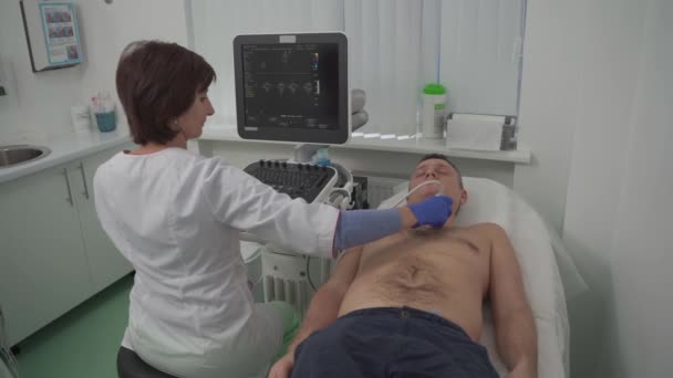 La doctora hace un chequeo cardíaco del hombre paciente usando equipos modernos en una clínica de cardiología. La cardióloga está examinando el corazón de la paciente con ultrasonografía, mirando la pantalla. Concepto sanitario — Vídeos de Stock