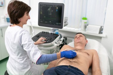 Doktor, erkek bir hastanın kalbini taramak için ultrason makinesi kullanıyor. Kardiyolog bir hastaya klinikte ekokardiyografi testi yapar. Hastanedeki hasta ultrason muayenesine alındı.