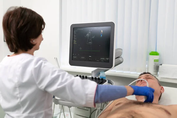 Woman doctor makes heart check of patient man using modern equipment in a cardiology clinic. Female cardiologist is screaning patient heart with ultrasonography, looking at screen. Healthcare concept — Stock Photo, Image