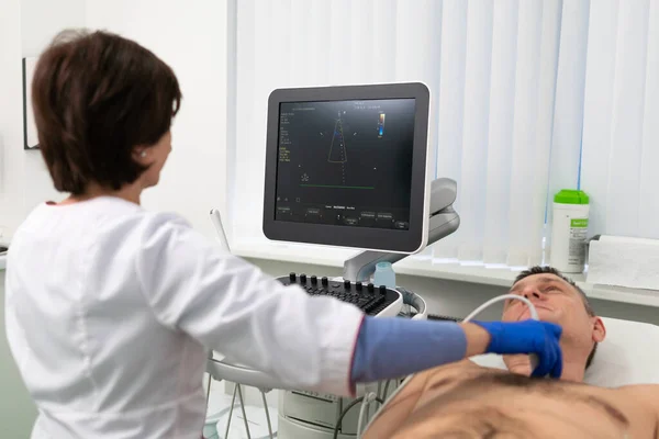 Doctor using ultrasound machine to scan heart of a male patient. Cardiologist makes a patient an echocardiographic test in a clinic. Patient under ultrasound examination in the hospital — Stock Photo, Image