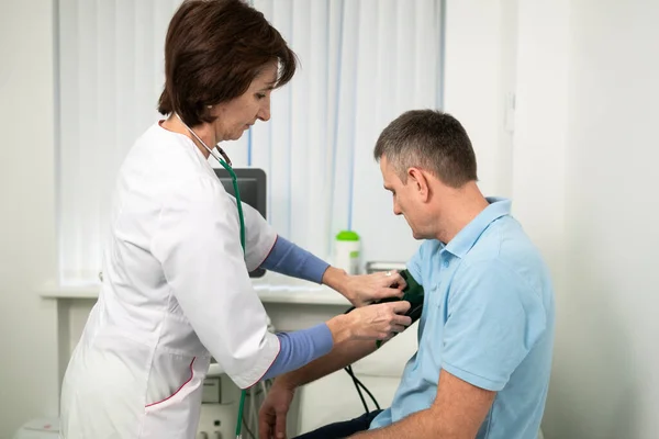 Concepto médico y sanitario. Hipertensión, presión arterial alta y precursores de accidentes cerebrovasculares en hombres de mediana edad. Chequeo médico. La doctora en medicina general mide la presión sobre el paciente en la clínica — Foto de Stock