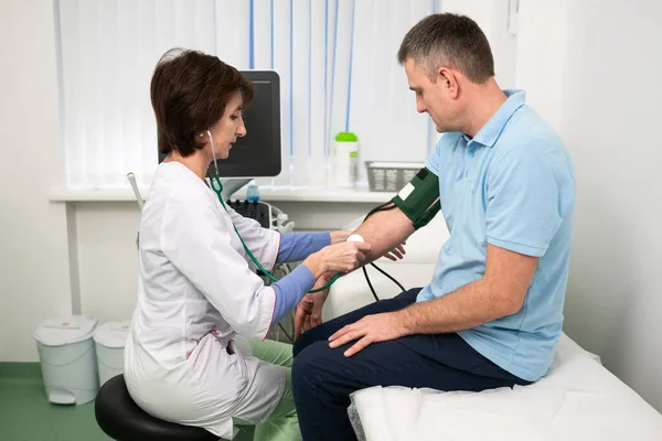 Concepto médico y sanitario. Hipertensión, presión arterial alta y precursores de accidentes cerebrovasculares en hombres de mediana edad. Chequeo médico. La doctora en medicina general mide la presión sobre el paciente en la clínica — Foto de Stock