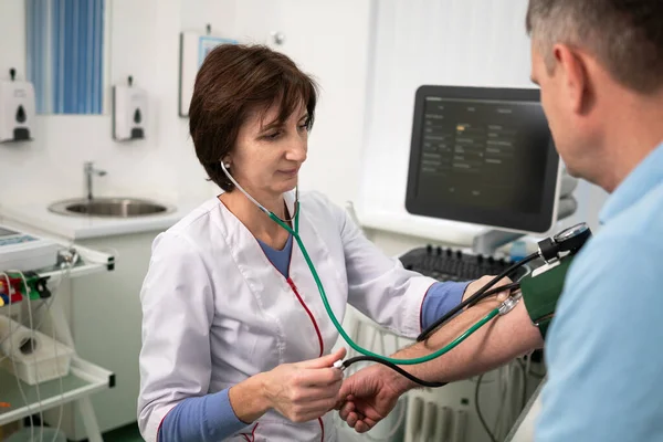 Concepto médico y sanitario. Hipertensión, presión arterial alta y precursores de accidentes cerebrovasculares en hombres de mediana edad. Chequeo médico. La doctora en medicina general mide la presión sobre el paciente en la clínica — Foto de Stock