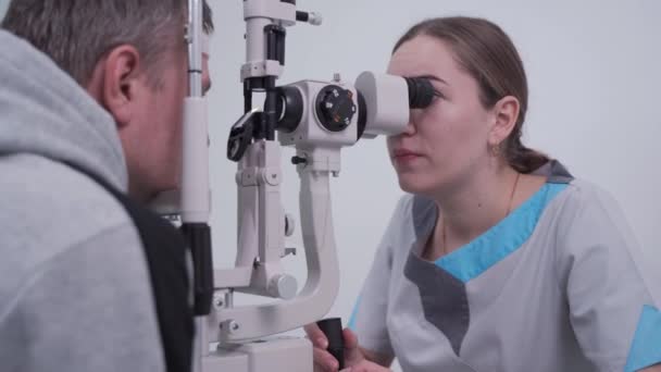 現代の眼科診療所で男性患者の目を調べる検眼医。現代の診療所で診察中の男性患者と目の医者。光学的概念。診療所での視力検査 — ストック動画