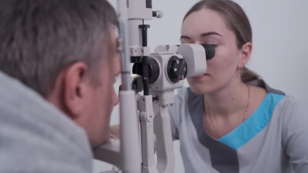 眼科クリニックの医師と患者。特別な眼の機器を持つ男性患者のチェックビジョン.光学的概念。男は光学者を訪れる。光または観光客のスリットランプの患者 — ストック動画