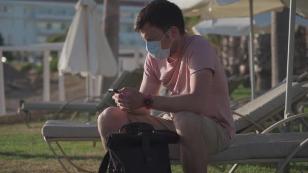 Summer vacation concept. Epidemic coronavirus covid-19 flu virus. New normal in vacation in time after COVID-19 pandemic. Sad masked man sits on sun lounger on the territory of an empty hotel — Video Stock