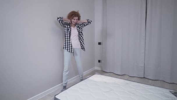 Temat przenosi się do nowego mieszkania i kupuje materac online dla komfortowego snu. Dojrzała kobieta jest szczęśliwa i testuje nowy materac na podłodze w pustym mieszkaniu. Zdrowy sen na materacu z pianki — Wideo stockowe