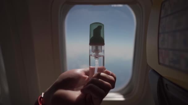 Une main d'homme tient un désinfectant pour les mains dans l'avion sur le fond d'une fenêtre par temps ensoleillé. Voyager pendant le concept d'épidémie de coronavirus. Antiseptique dans les transports publics. Nouvelle normalité — Video