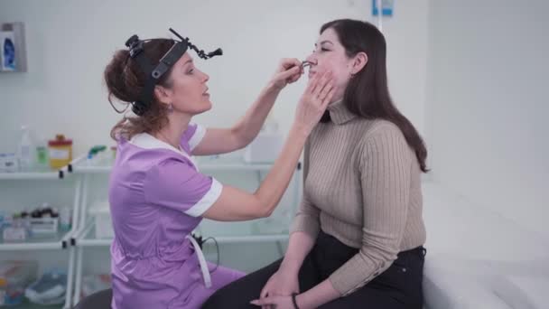 Otolaryngologi koncept. Positiv kvinna otorhinolaryngologist kontrollera näsa med otoscope av hans patient på sjukhuset. Nästäppa, bihåleinflammation, allergikoncept. Kvinnlig patient på modern ENT klinik — Stockvideo