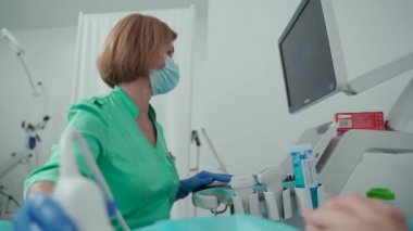 Hastanedeki kadın ziyaretçi doktor. Hasta profesyonelce muayene edilir. Karnı ultrasonla kontrol ediliyor. Korunan yüz maskesi takan jinekolog kadın ultrasonu ve ultrason prosedürü uygular.