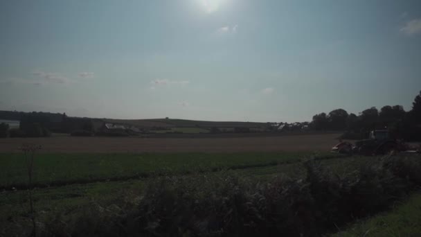 Harvesting machine works in a field in northern France in the Brittany region. Harvesting cereals and legumes on large plantations using agricultural machinery. Tractor ploughing field. Agribusiness — стоковое видео