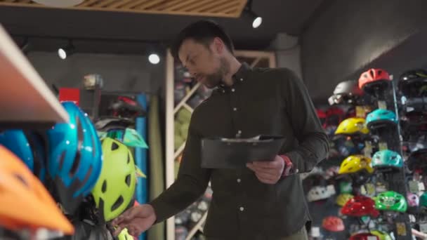 Bike shop manager controlla le informazioni sul prezzo del casco su tablet, venditore fa un inventario in negozio di sport. Tema della piccola impresa che vende biciclette. Lista di controllo documento venditore in mano nel negozio di biciclette — Video Stock