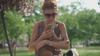 Sahibi ve hayvan birbirlerine olan sevgilerini gösteriyorlar. Elbiseli ve güneş gözlüklü olgun bir dişi yazın güneşli bir havada şehir parkında bir bankta otururken kollarında bir daksund köpeğine sarılıyor.