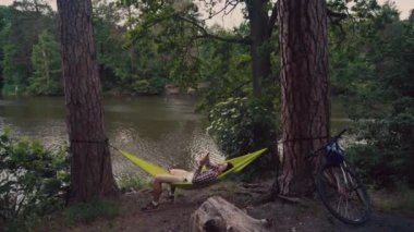 Yeşil hamakta dinlenen bisikletli bir adam gölün yakınlarındaki bir ormanda akıllı telefondan internette sörf yapıyor. Nehir kenarındaki hamakta bisiklet kullanan biri telefon kullanıyor. Erkek ormana bisikletle gelir ve hamakta dinlenir.