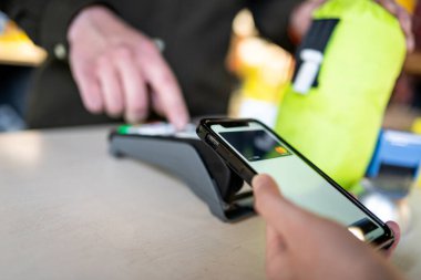 Cep telefonu ödemesiyle alışveriş. Müşteri temassız ödeme yapıyor. NFC teknolojisiyle çalışan bir kadın. Dijital cüzdan ile irtibatsız ödeme. NFC ödeme terminalinde kart ile öde.