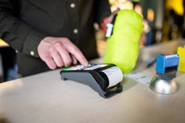Satış elemanı ödeme terminalini elinde tutarken satın alma makbuzunu da tutuyor. Eller yukarı. NFC, iş ve banka işlemleri kavramı. Kağıt bant ile ödeme terminali. Banka terminali.