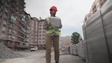 Erkek bir inşaat yöneticisi inşaat alanındaki belgelerle inşaat matralini kontrol ediyor. İş yerindeki bir inşaat alanında müfettiş izolasyonlu briketleri inceliyor.