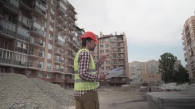 Erkek müteahhit inşaat alanına inşaat malzemesi getirip, malzemeleri kontrol etmeyi düşünüyor. Müfettiş inşaat malzemelerini kontrol edip sayıyor. Evler için izolasyon denetleyicisi