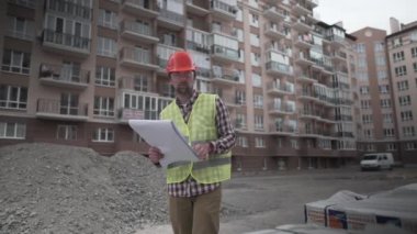 Erkek müteahhit inşaat alanına inşaat malzemesi getirip, malzemeleri kontrol etmeyi düşünüyor. Müfettiş inşaat malzemelerini kontrol edip sayıyor. Evler için izolasyon denetleyicisi