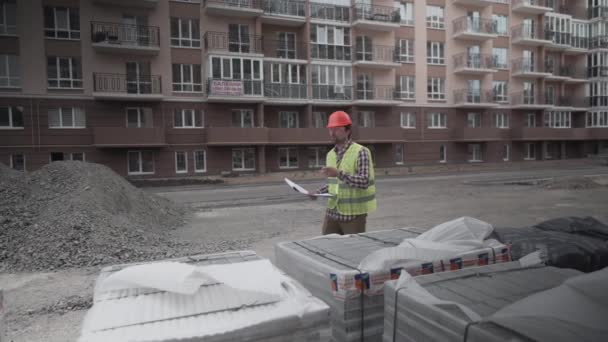 Mannelijke bouwer overweegt gebracht bouwmateriaal op de bouwplaats, controleert materialen. Inspecteur controleert en telt bouwmateriaal op locatie. Inspecteur Inspectie isolatie van huizen — Stockvideo