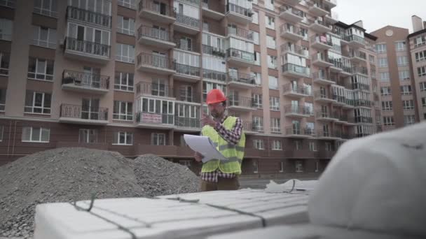 Męski kierownik budowy sprawdza ilość i sprawdza matrycę budowlaną z dokumentami na placu budowy. Inspektor na budowie w pracy bada brykiety z izolacją — Wideo stockowe