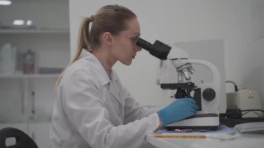 Laboratuvarda mikroskop analizi yapan üniformalı kadın doktor. Laboratuvarda çalışan bir bilim adamı. Modern tıp laboratuarında teknolojik ekipmanlarla çalışan mikrobiyolog kadın.