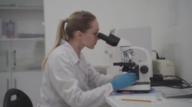 Tıbbi laboratuvarda mikroskop arkasında numune ve analizlerle çalışan kadın tıbbi çalışmalar. Kadın laboratuvar teknisyeni hastanede mikroskopla örnek analiz ediyor. Tıp, mikrobiyoloji