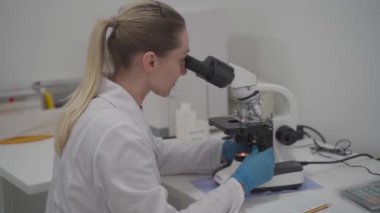 Laboratuvarda çalışırken mikroskop kullanan kadın bir bilim adamı. Modern tıbbi araştırma laboratuarı. Mikroskop incelemesi yapan kadın laboratuvar asistanı biyokimyasal maddeler, kan testleri...