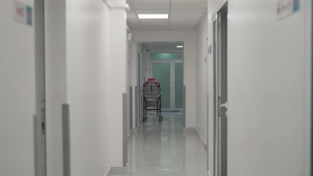 Üres kórházi ágy egy üres modern klinika folyosóján. Stretcher a kórház folyosóján. Ágy betegek szállítására a kórház folyosóján. Orvosi hordágy az átjáróban — Stock videók