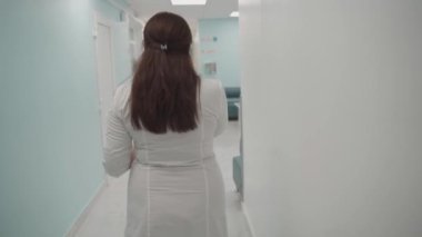 Beyaz önlüklü kadın doktor elinde hasta kartı ya da belgelerle kliniğin koridorunda yürüyor ve telefonla konuşuyor. Hastanedeki hasta çizelgesini okurken sağlık uzmanı telefon görüşmesi yapıyor.