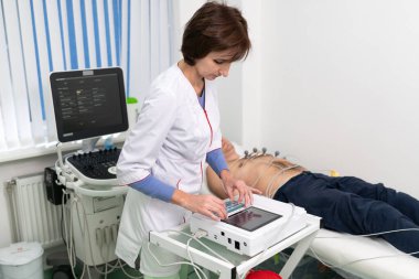 Kardiyolog doktor hastanede kanepede yatan adama elektrokardiyografi uyguluyor. Modern klinikteki erkek EKG testi. Teşhis, sağlık, sağlık hizmetleri. Hastane hastası ve EKG testi.