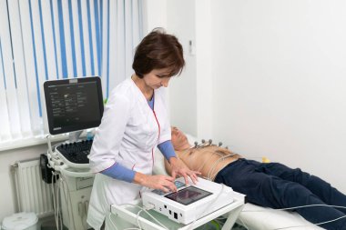 EKG konsepti. Kadın kardiyolog, kardiyoloji kliniğindeki hastaya elektrokardiyogram testi yapıyor. Tıp, kardiyoloji, kalp konseptinin EKG 'si. Tıbbi testlerde erkek..