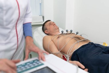 Elektrokardiyogram için tıbbi ekipman. Erkek hastaya EKG testi yapan doktorlar. Kalp krizi teşhisi, taşikardi. Elektrokardiyografi prosedürü. Kardiyolog kontrol testi yapıyor..