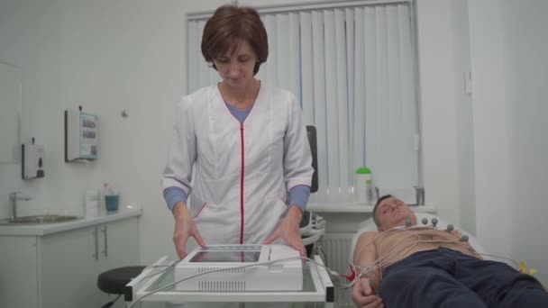 EKG-koncepció. Női orvos kardiológus elektrokardiogram vizsgálatot végez férfi betegen a kardiológiai klinikán. Gyógyszer, kardiológia, EKG a szív koncepció. Férfi az orvosi vizsgálaton — Stock videók