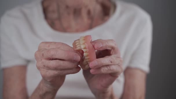 Topic of orthodontics, the lack of a chewing apparatus in the elderly. Close-up of a senior 90-year-old woman holding a raised jaw in her hands, a dental prosthesis in the hands of an elderly patient — Stock Video