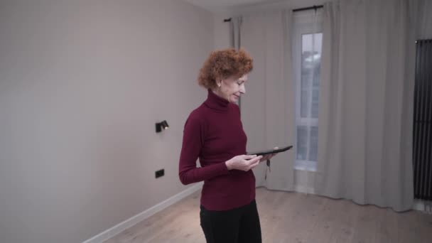 A vendég végzős nő ellenőrzi az üres lakást. Érett nő vizsgálja ingatlan bérleti lehetőségek. Nő vizsgálja építészeti terv és megvizsgálja a dokumentumokat, mielőtt vásárol egy lakást — Stock videók