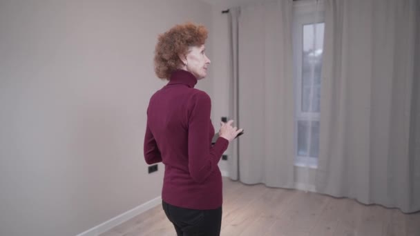 백인 여성은 임대 계약서에 서명하기 전에 빈 아파트를 조사한다. 한연로 한 여자는 계약을 맺기 전에 아파 아트 를 살펴보고 있다. 고객들 이 apartmnet 을 확인하고 있습니다 — 비디오