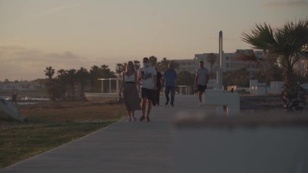 Ciprus. Pathos vagyok. 2021. május 15. Este sétány pálmafákkal és egy sétány mentén a szállodák közelében a tenger és az emberek sétálnak. Mediterrán üdülőhely naplementekor. — Stock videók