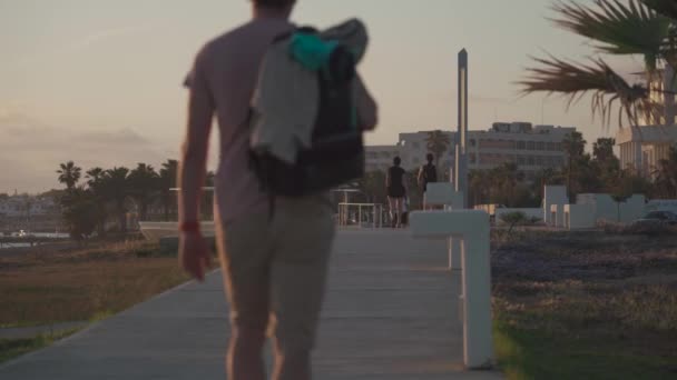 Cypr. Pathos. 15 maja 2021. Wieczorna promenada z palmami i promenadą wzdłuż hoteli w pobliżu morza i ludzi spacerujących. Śródziemnomorski kurort w czasie zachodu słońca. — Wideo stockowe