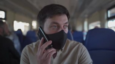 Maske takan ve toplu taşımada telefonla konuşan bir adam. Siyah maskeli bir erkek işe giderken trende cep telefonuyla konuşuyor. Yeni normal, enfeksiyon, virüs ve alerjilere karşı kendini koruma