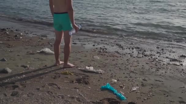 El hombre irreconocible se para con la espalda en la playa, mira al mar con una botella de plástico en sus manos en una pila de basura de plástico clavada en la playa de Chipre. Concepto de conservación ambiental — Vídeo de stock