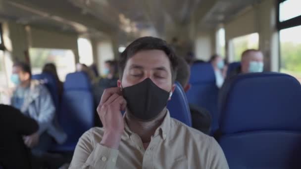 Man in koptelefoon die in slaap valt in de trein en gezichtsmasker draagt tijdens een coronavirus pandemie. Gemaskerde man met behulp van draadloze in-ear hoofdtelefoon tijdens het inslapen op een lange treinrit — Stockvideo