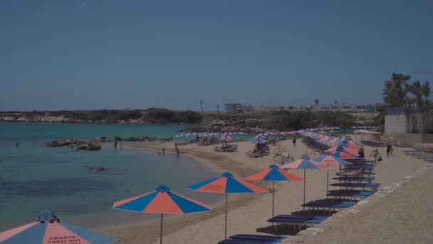 20 Μαΐου 2021 Κύπρος, Πάφος. Κόραλ Μπέι. Ομπρέλες παραλίας και ξαπλώστρες με παραθεριστές σε αμμώδη παραλία κοντά στη Μεσόγειο θάλασσα στο νησί Κύπρος σε ηλιόλουστο καιρό — Αρχείο Βίντεο