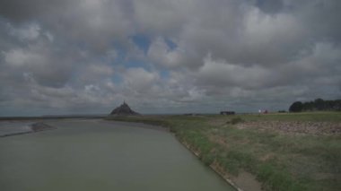 Kuzey Fransa 'nın Normandiya bölgesindeki Mont Saint-Michel Manastırı' nın kalesine yürüyen turistlerle dolu Cuenon Nehri ve yol.