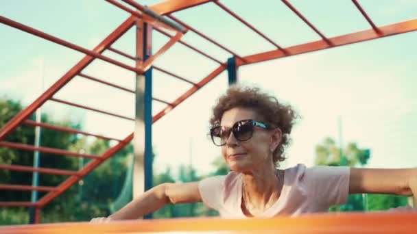 Zůstaňte aktivní v důchodu. Radostná stárnoucí žena dělá kliky na bradě baru venkovní tělocvičny. — Stock video