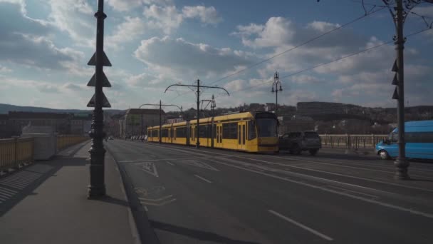 8 Maret 2022, Hungaria, Budapest. Temanya adalah transportasi umum dan sistem kereta api di Budapest. Sebuah trem kota kuning biasa melewati jalan-jalan utama Budapest dalam cuaca musim semi yang cerah — Stok Video