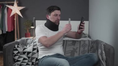 Boyunluk ve boyun yaralanması olan hastaya çevrimiçi video konsültasyonu yapılıyor ve elinde haplar bulunuyor. Köpüklü tasmalı bir adam travma uzmanını arıyor ve ilaçlarını telefonda gösteriyor.